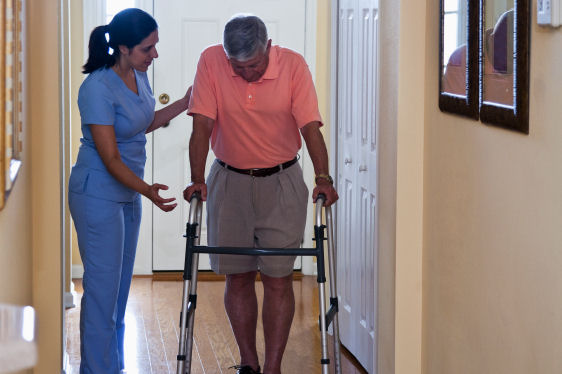 Home haaealthcare - Hispanic nurse at home of senior man (60s) using walker.